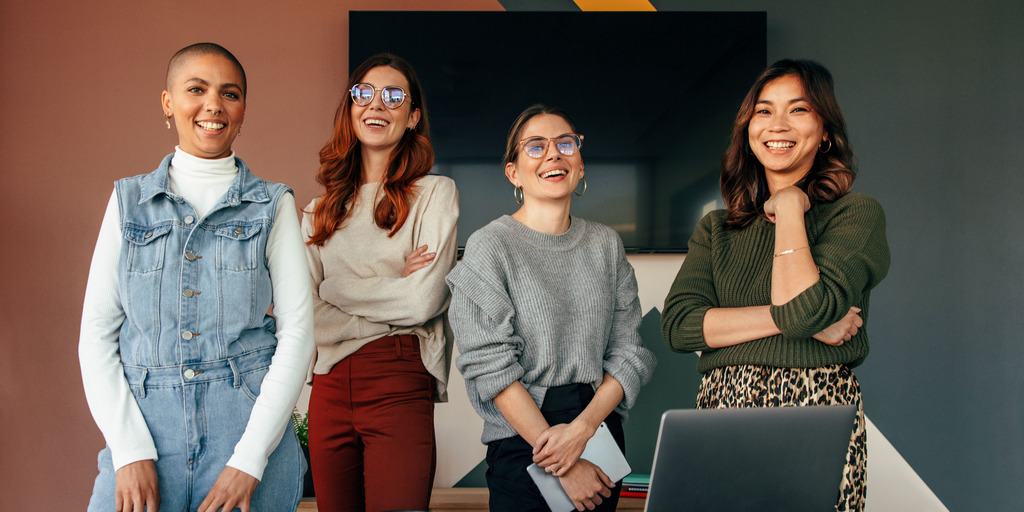 Successful female entrepreneurs smiling cheerfully while standing behind a table in a boardroom. Group of multicultural businesswomen working together in a modern office