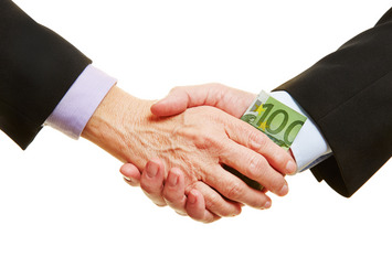Zwei Politiker oder Geschäftsleute im Anzug geben sich die Hand, einer von ihnen hat dabei einen 100-Euro-Schein in der Hand.