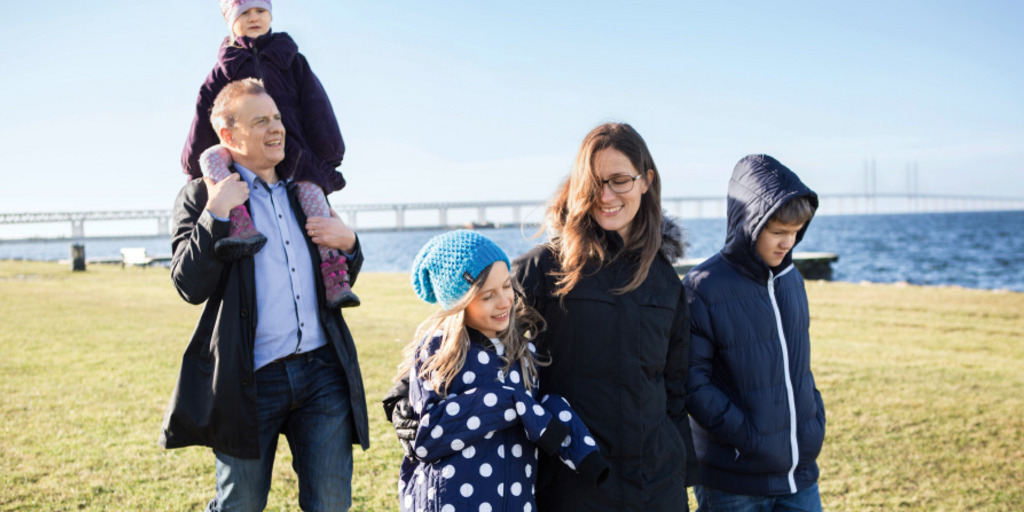 Eine Familie geht am Strand von Malmö in Schweden spazieren. Im Hintergrund sieht man die Öresundbrücke, die nach Kopenhagen führt.