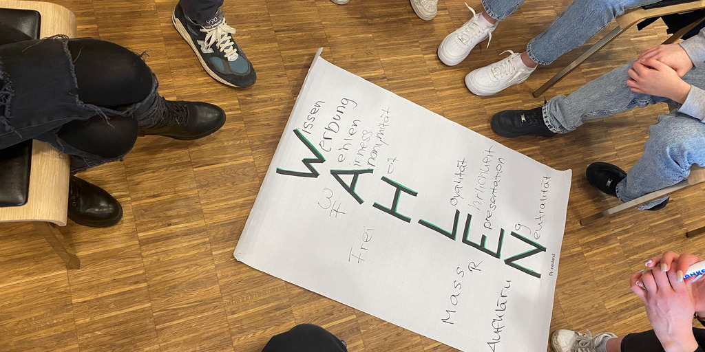 Junge Menschen um ein Plakat mit der Aufschrift Wahlen