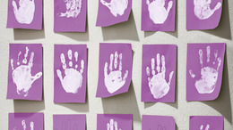 Zu sehen sind die weißen Handabdrücke von Kindern auf einem lilafarbenem Hintergrund.