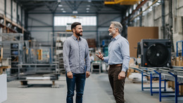 Zwei Männer stehen in einer Werkshalle und unterhalten sich