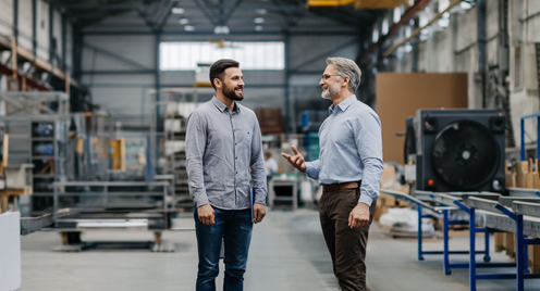 Zwei Männer stehen in einer Werkshalle und unterhalten sich