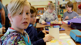 Schulkinder sitzen im Klassenraum und bearbeiten eine Schulaufgabe.