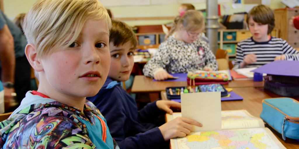 Schulkinder sitzen im Klassenraum und bearbeiten eine Schulaufgabe.