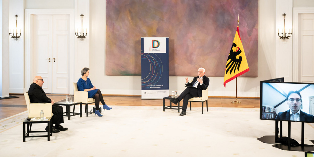 Bundespräsident Frank-Walter Steinmeier diskutiert mit den übrigen Teilnehmer:innen des Forum Bellevue im Großen Saal des Schloss Bellevue. Ben Scott ist online zugeschaltet und auf einem großen Bildschirm im Saal sichtbar. Armin Nassehi und Margrethe Vestager sitzen auf Stühlen neben dem Bundespräsidenten.