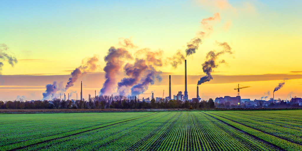 Qualmende Industrie vor grünem Feld