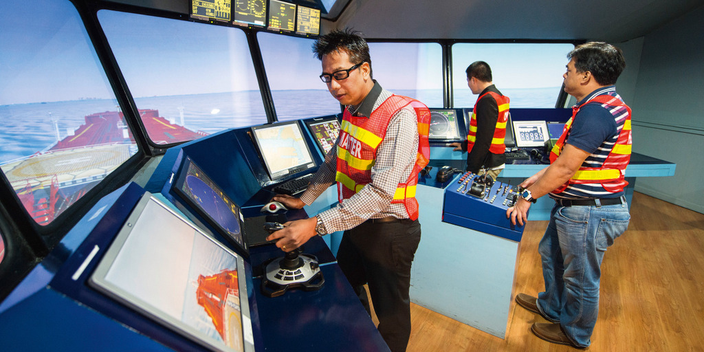 Mehrere Arbeiter stehen auf einer Simulationsbrücke eines Trainingscenters für Seeschifffahrt.