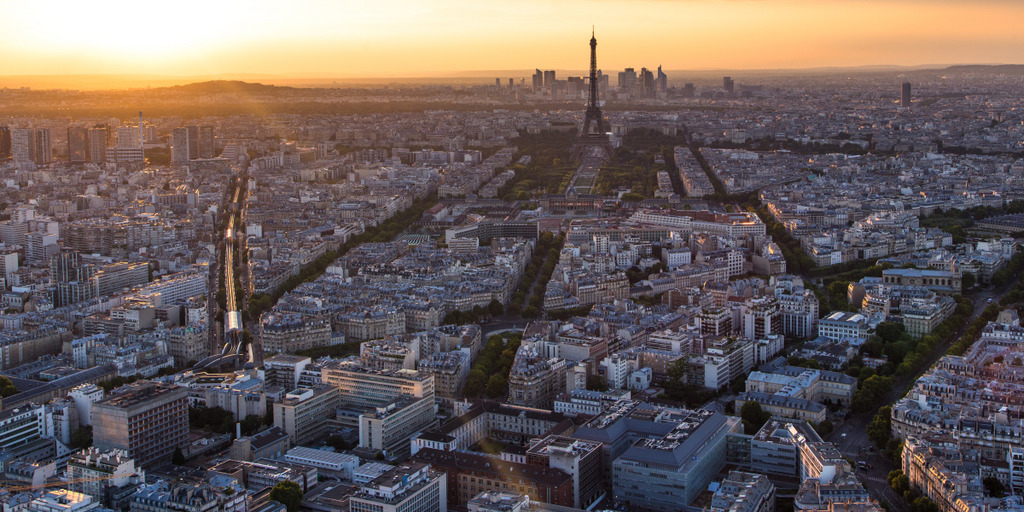 [Translate to English:] Blick auf Paris mit Eifelturm. Die Stadt liegt im Licht der aufgehenden Sonne.