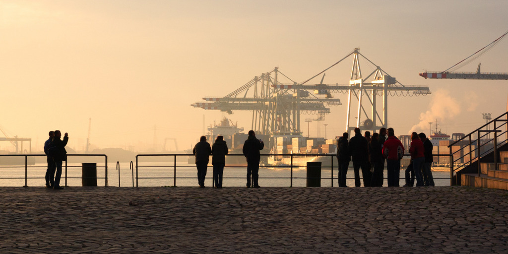 In Hamburg stehen einige Touristen am Ufer der Elbe und blicken auf die Containerkräne des Hamburger Hafens am anderen Ufer der Elbe.