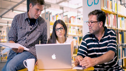 [Translate to English:] Drei Personen in einer Arbeitsgruppe vor einem Laptop in einer Bibliothek.