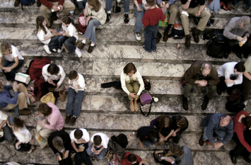Viele Menschen, die in Gruppen auf Treppen sitzen. In der Mitte sitzt eine Person allein.