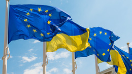 Ukraine and European Union flags on poles fluttering by wind on blue sky.