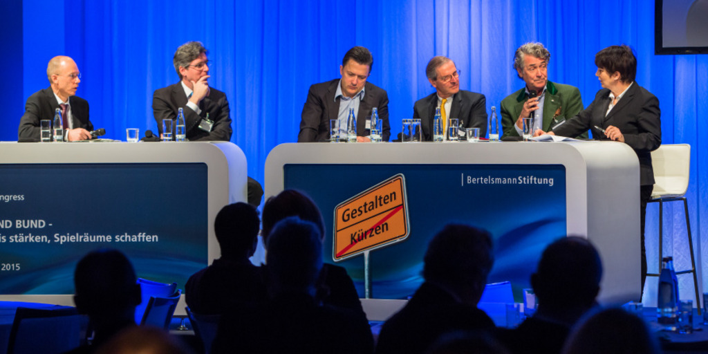 Eine Diskussionsrunde beim Kommunalkongress 2015 in Berlin: Die Teilnehmer der Diskussion sitzen an zwei Tresen auf einem Podium
