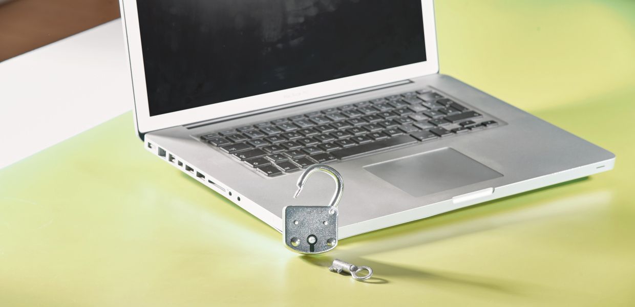 (© Jan Voth/Bertelsmann Stiftung - CC BY-SA 4.0 https://creativecommons.org/licenses/by-sa/4.0) Ein aufgeklappter Laptop steht auf einem grünen Tisch. Davor lehnt ein geöffnetes Messingschloss am Laptop.