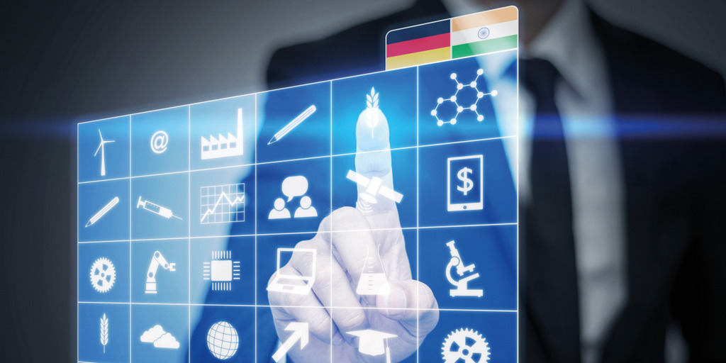 A business man taps a touchscreen on which icons symbolizing different economic branches and the flags of Germany and India are displayed.