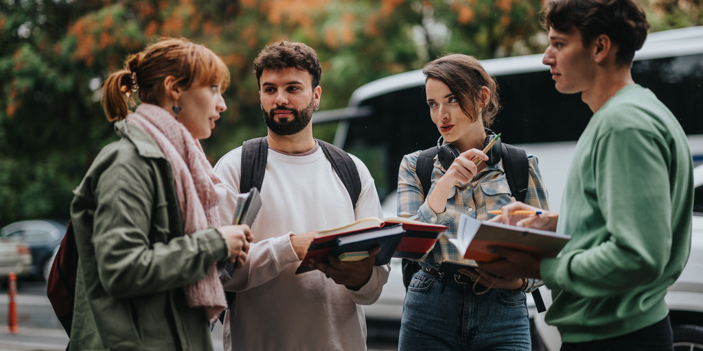 Ein Gruppe junger Studenten mit Rucksäcken und Notebooks in den Händen, befinden sich in einer Diskussion.