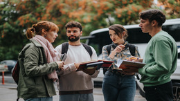 Ein Gruppe junger Studenten mit Rucksäcken und Notebooks in den Händen, befinden sich in einer Diskussion.