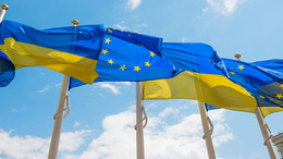 Flags of Ukraine and the EU are flying on flagpoles next to each other.