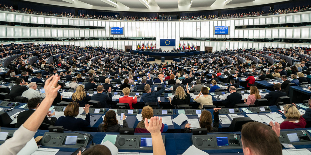 Das Europäische Parlament in Straßburg während einer Abstimmung im April 2019. Zu sehen ist der gesamte Plenarsaal mit den voll besetzten Abgeordnetenreihen. Einige Abgeordnete geben ihre Stimme ab, indem sie ihre rechten Hände erheben.
