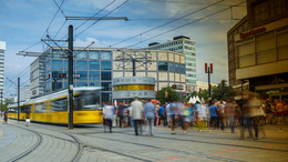 Aufnehme der Weltuhr am Alexanderplatz in Berlin. Davor sieht man eine verschwommene Menschenmenge und eine Tram.