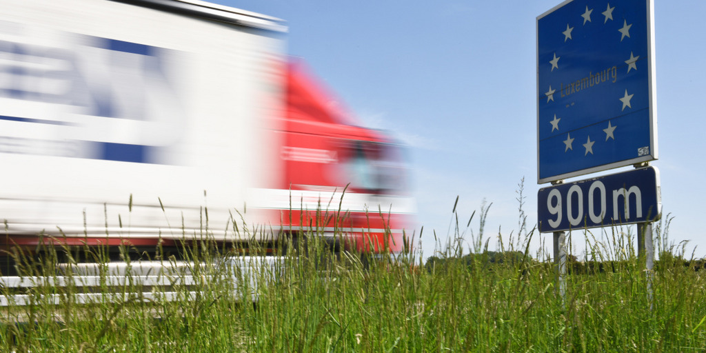 A road sign carrying the twelve stars of the European flag shows that the border of Luxembourg is located 900 meters away. A truck passes the sign.