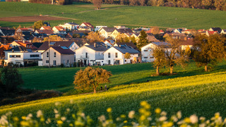 Blick über Felder und Bäume auf eine ländlich gelegene kleine Gemeinde in Deutschland.