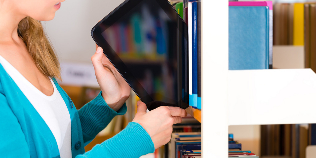 Eine junge Frau stellt einen Tablet-Computer in ein Bücherregal.