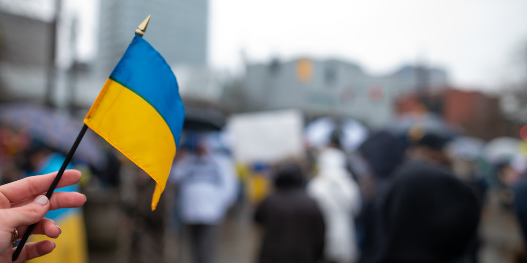 Hand mit Ukrainischer Flagge im Hintergrund sind Menschen