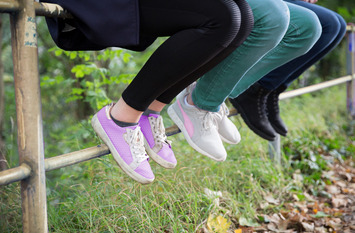 Drei Jugendliche, von denen nur die Beine und Schuhe zu sehen sind, sitzen nebeneinander auf einem Geländer.