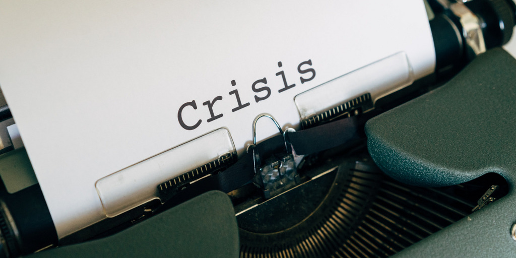 A sheet of paper can be seen inserted in a typewriter. Someone has typed the word "crisis" on the sheet of paper.