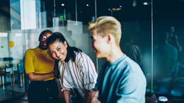 Drei lachende junge Menschen in einem Büro.