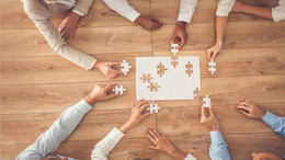 Business people sitting at office desk, putting puzzle pieces together, finding solution, high angle view.