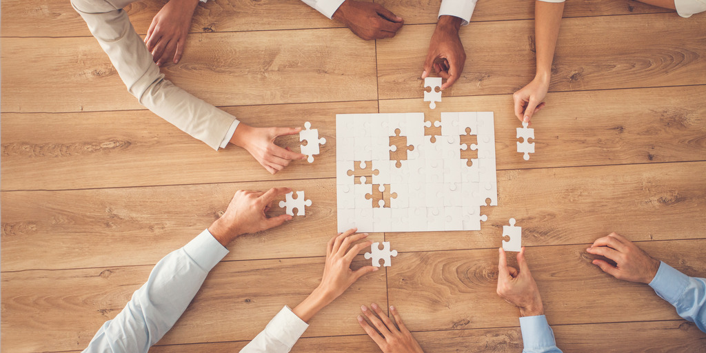 Business people sitting at office desk, putting puzzle pieces together, finding solution, high angle view.