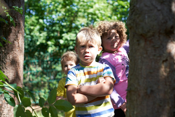 Mehrere Kinder stehen zusammen. Sie stehen im Wald. Das vorderste Kind verschränkt die Arme.