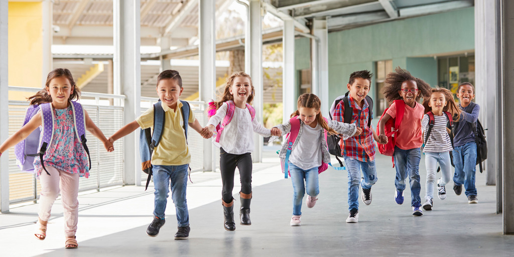 Grundschulkinder rennen händchenhaltend durch den Korridor.