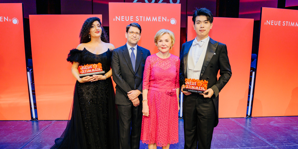 -	Liz Mohn, Präsidentin des Wettbewerbs und Vorsitzende des Vorstands der Liz Mohn Stiftung, zusammen mit Alexander Neef, Juryvorsitzender der NEUEN STIMMEN, und den Erstplatzierten des Wettbewerbs 2026, Arpi Sinanyan und Jiazhou Wang