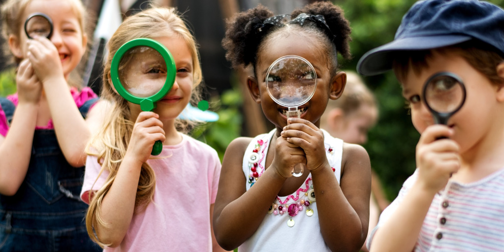 Gruppe von Kindergartenkindern, die mit einer Lupe auf Entdeckungsreise gehen.