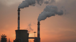 zwei rauchende Schornsteinschlote einer Industrieanlage in der Abenddämmerung