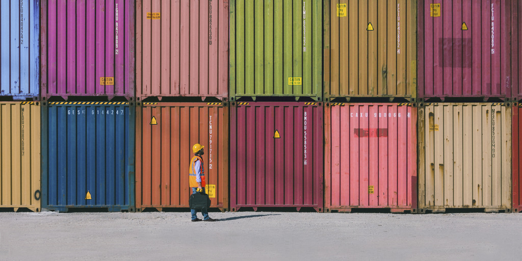 Engineer man with yellow crash helmet and worker west checking cargo freights in front of colorful cargo contrainer stacks in shipping port