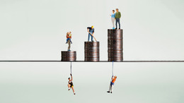 Drei Münzstapel und Miniaturmenschen symbolisieren das wirtschaftliche Ungleichgewicht.