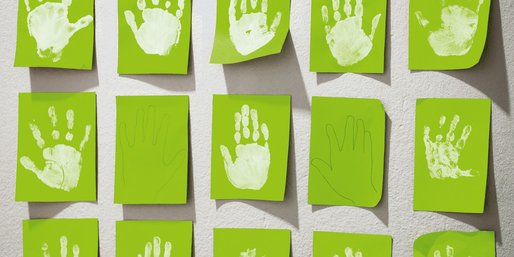 hellgrüne Post-It-Zettel kleben an einer Wand. Auf einigen von den Zetteln sind Hände abgebildet.