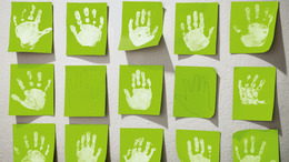 hellgrüne Post-It-Zettel kleben an einer Wand. Auf einigen von den Zetteln sind Hände abgebildet.