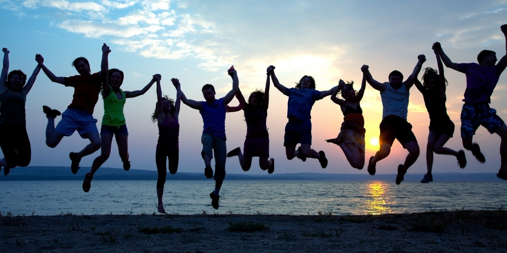 Gruppe junger Menschen hüpft fröhlich am Strand in die Luft.