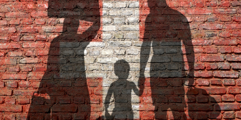 Backsteinmauer in den Farben der schweizerischen Flagge. Darauf zu sehen die Schatten einer Frau, eines Jungen und eines Mannes.