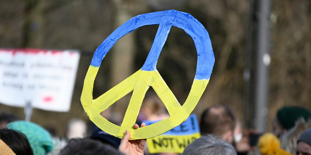 Bei einer Demonstration gegen den Krieg in der Ukraine am Brandenburger Tor in Berlin hält eine Person ein Friedens-Symbol in den Farben der ukrainischen Flagge, Blau und Gelb, in die Höhe.