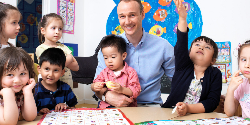Stefan Hensel, Gründer und Geschäftsführer der Hamburger PEDIA gGmbH und damit Träger einer der wenigen chinesischen Kindergärten in Deutschland, sitzt mit einigen Kindern in seinem Kindergarten.