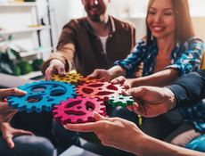 Junge Menschen halten bunte Zahnrädchen, die ineinander greifen.