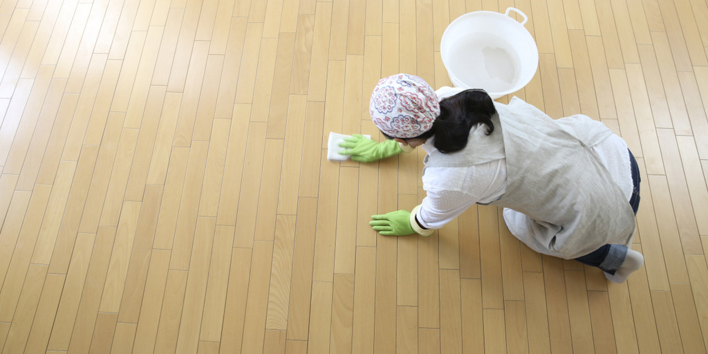 Eine Putzfrau wischt auf den Knien alleine einen großen Pakett-Fußboden