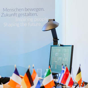 Moderator vor dem Bildschirm, im Vordergrund europäische Flaggen